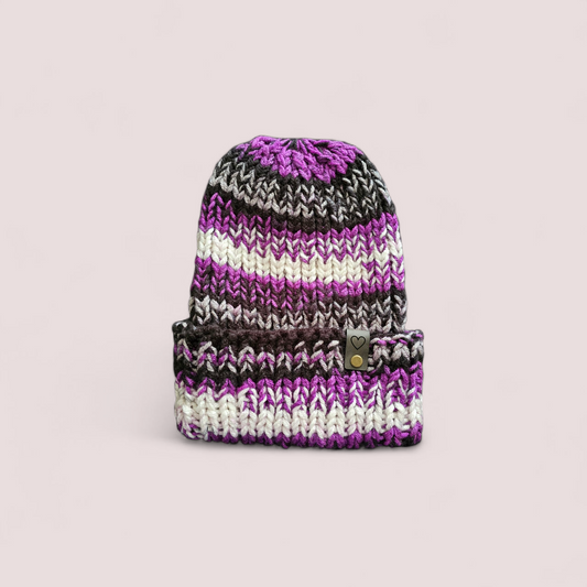 Knitted beanie with purple, black, and white stripes on a light gray background