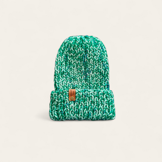 Green knitted beanie with a brown tag on a beige background